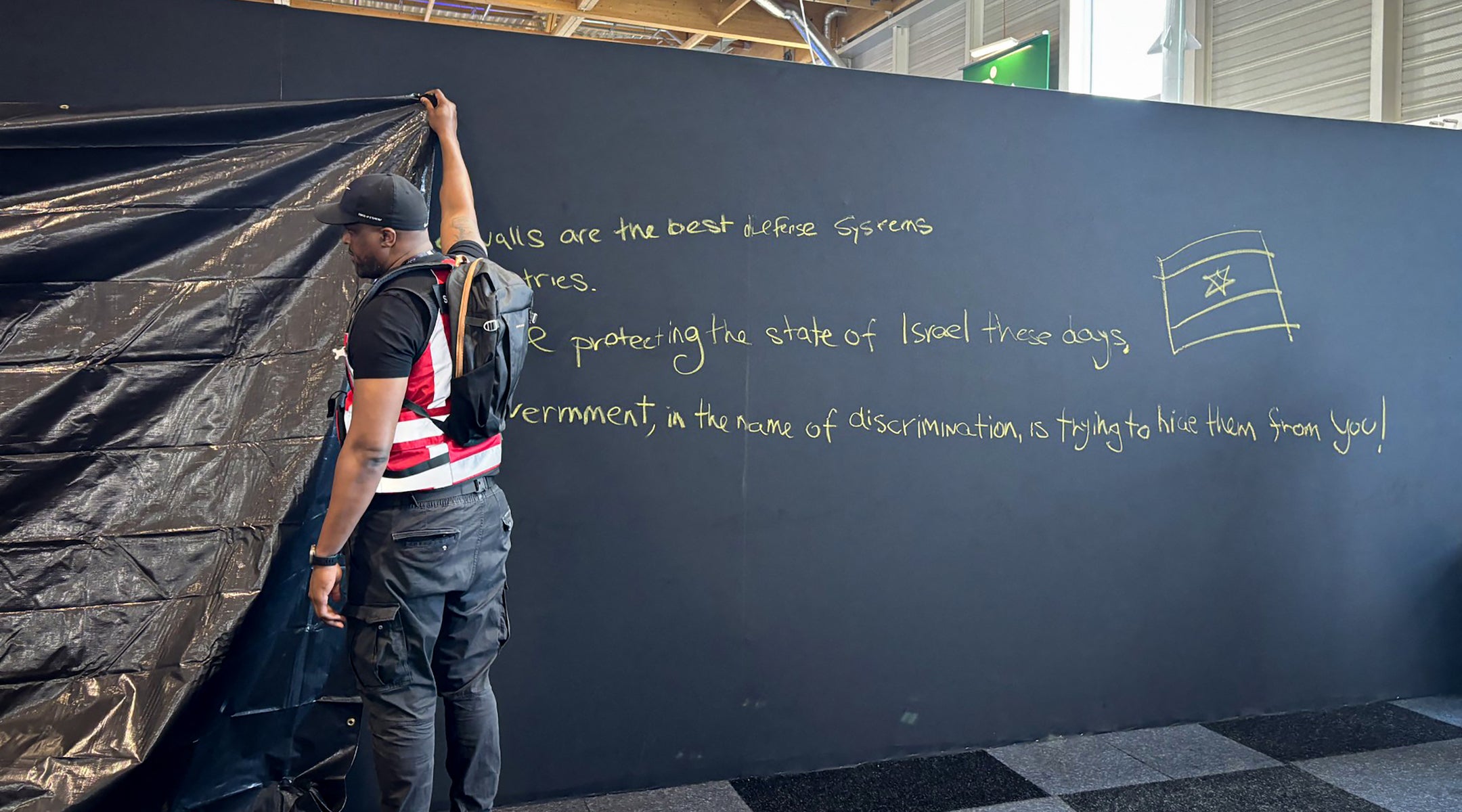 A security personnel works to hide a graffiti reading "Behind these walls are the best defense systems used by many countries. These systems are protecting the state of Israel these days. The French government, in the name of discrimination is trying to hide them from you!", on a panel of the Israel Aerospace Industries (IAI) Israeli Pavillon during the International Paris Air Show at the Le Bourget Airport on June 16, 2025.