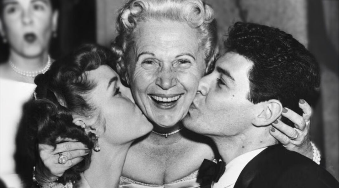 Jennie Grossinger, proprietor of Grossinger's Catksills Resort, is flanked by Debbie Reynolds and Eddie Fisher, who are both kissing her on her cheeks