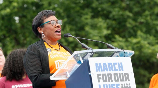 NEA president rebecca pringle speaking in an orange shirt at a podium.