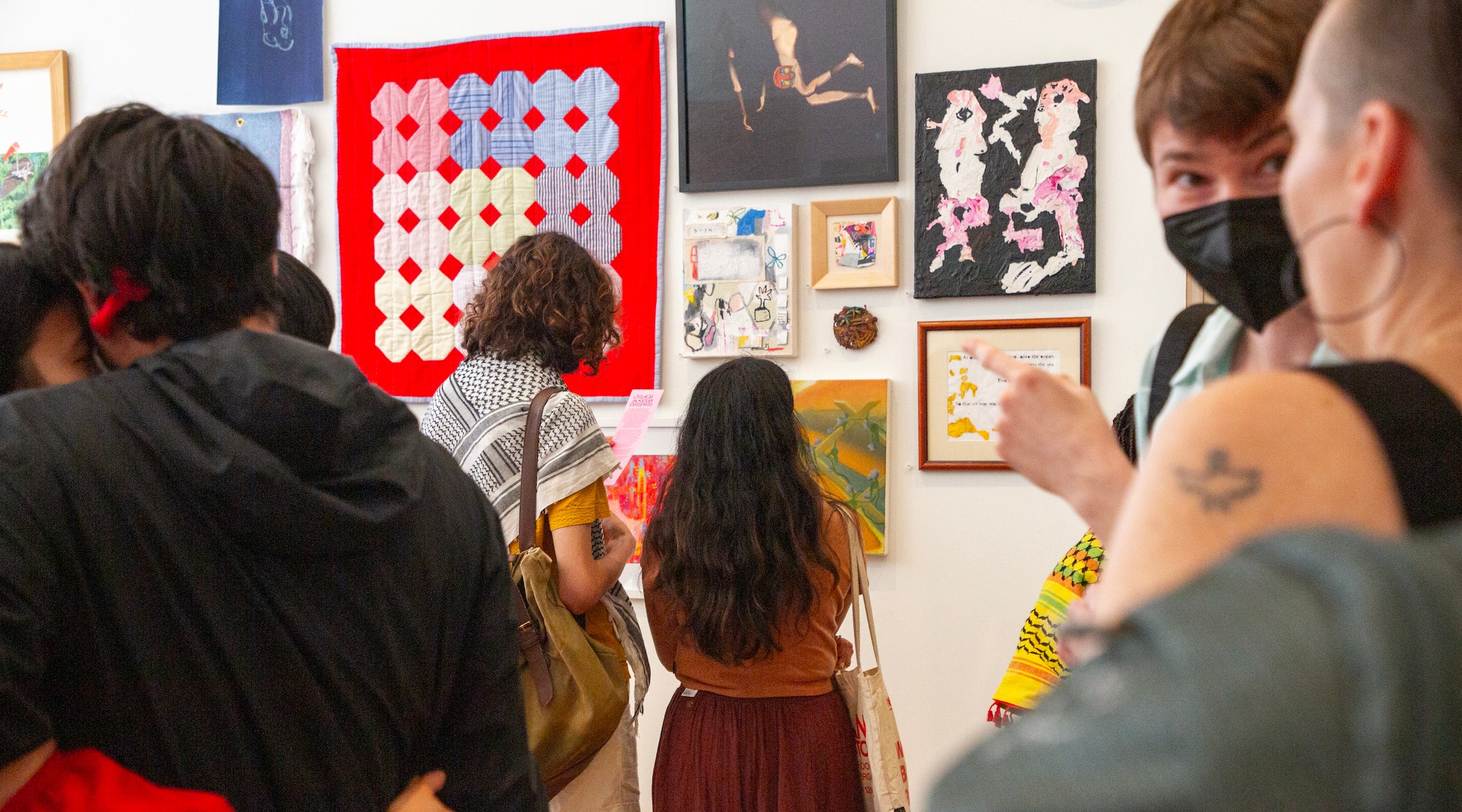 A photo of people looking at paintings on a wall.