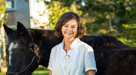 A photo of Geraldine Brooks in front of a horse.