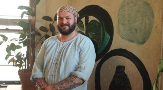 A photo of Gabriel in a light blue shirt standing in front of a painting.