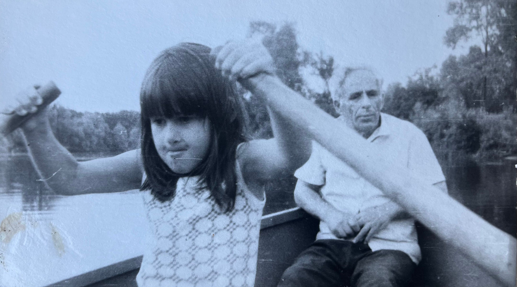 A young girl rows a boat as her grandfather looks on.