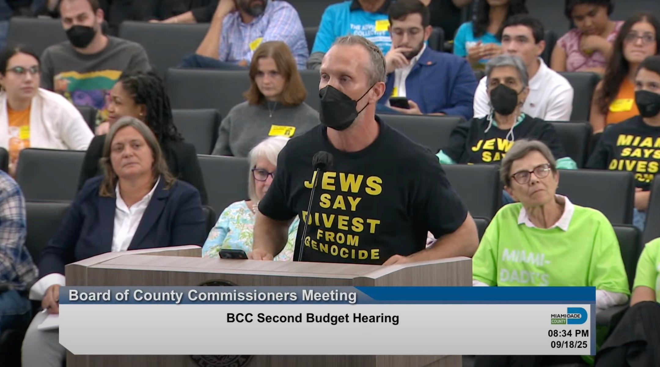 A protester wearing a "Jews Say Divest From Genocide" gives public comment at a meeting
