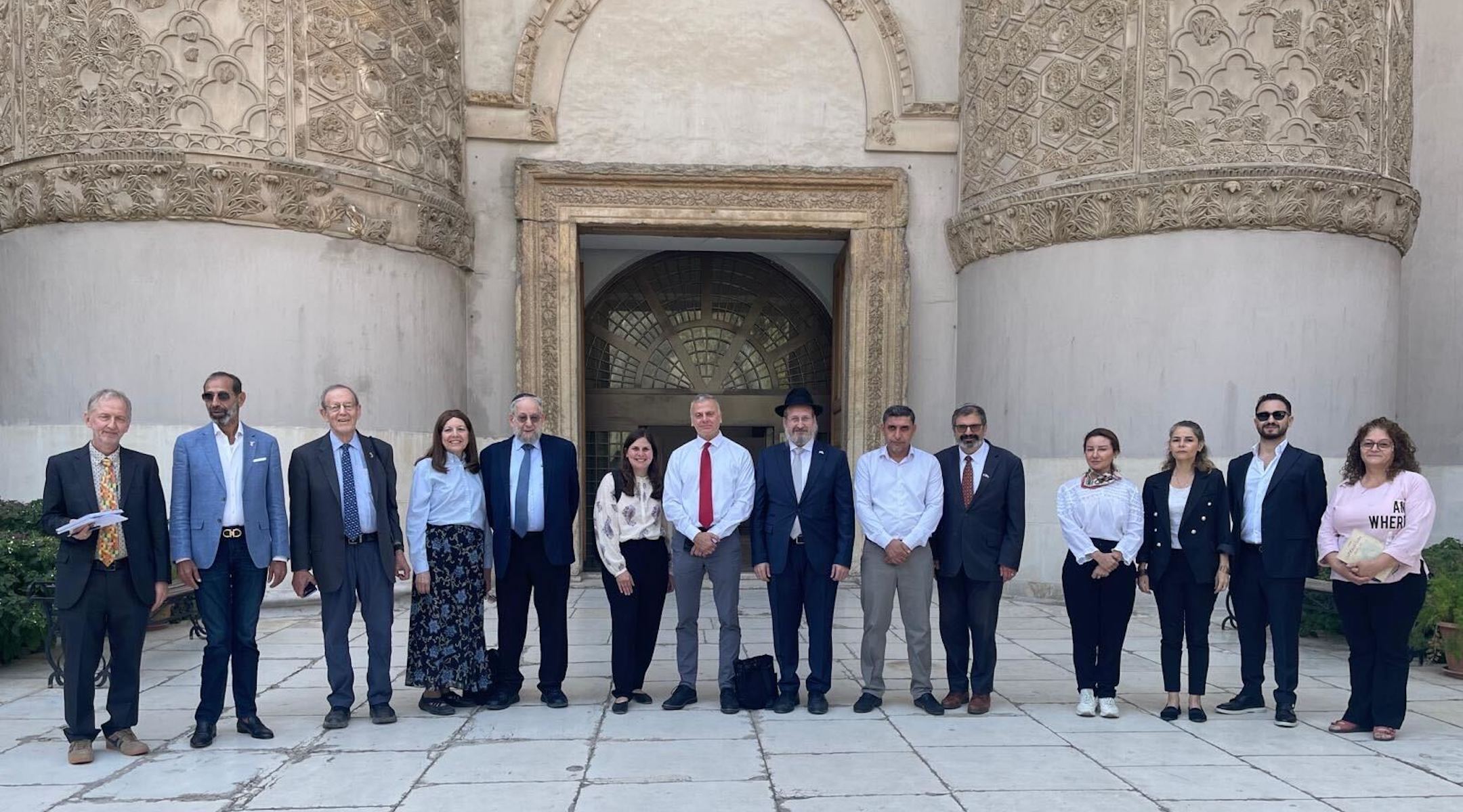 The group of delegates stand in a line in front of the museum's facade.