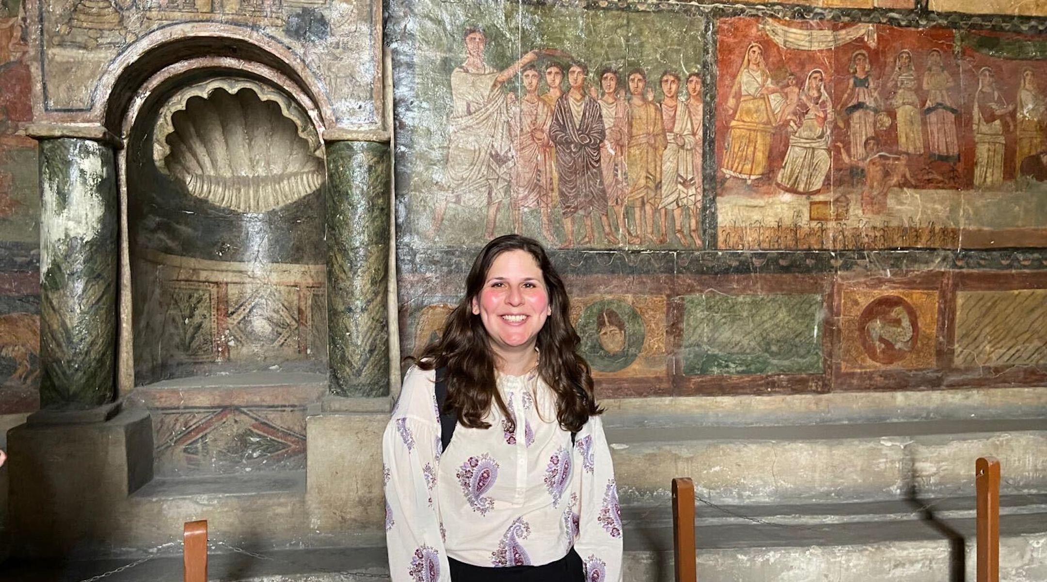 A photo of Jill smiling in front of the Dura Europos paintings.