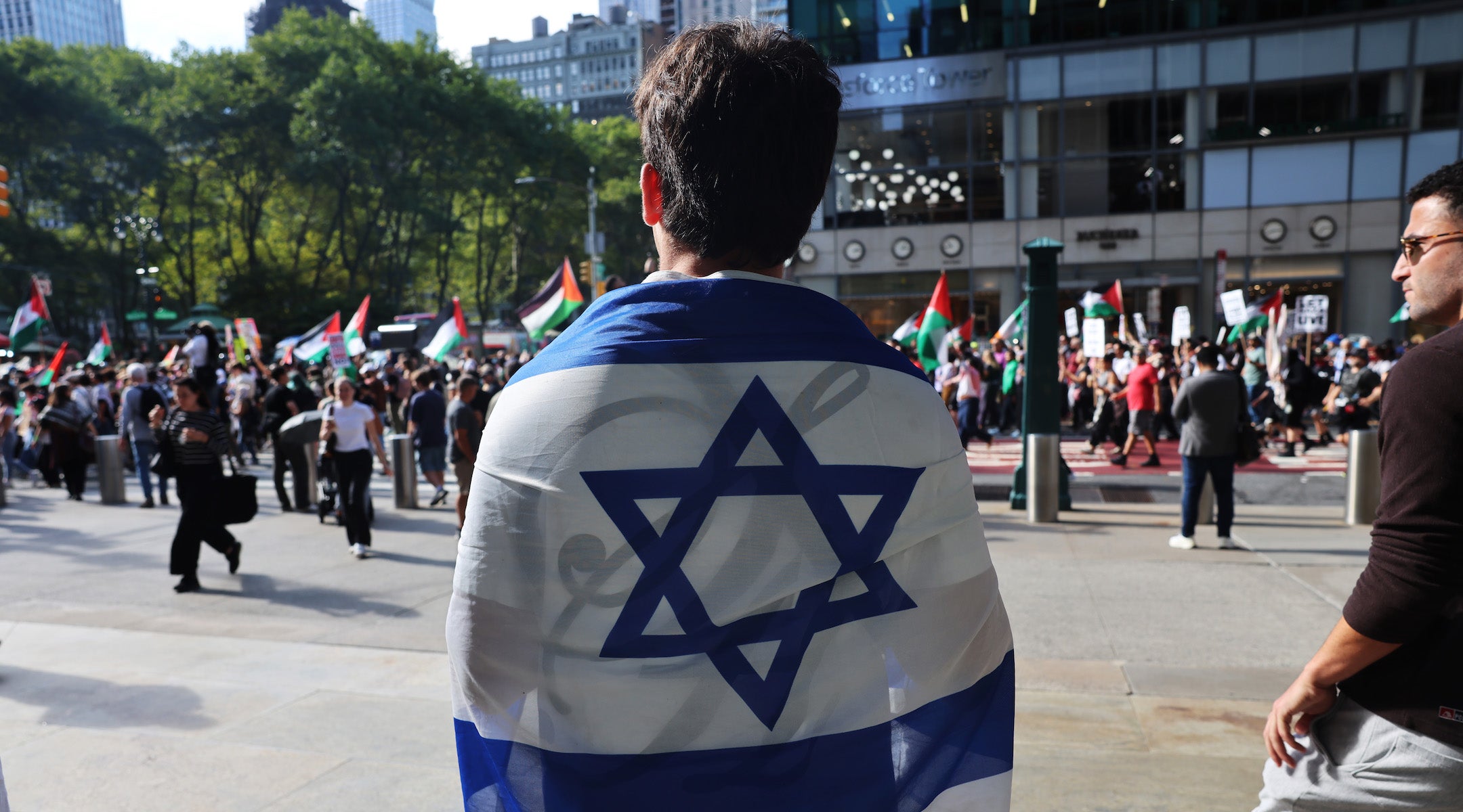 A photo of a man wearing an Israeli flag across his back in the street.