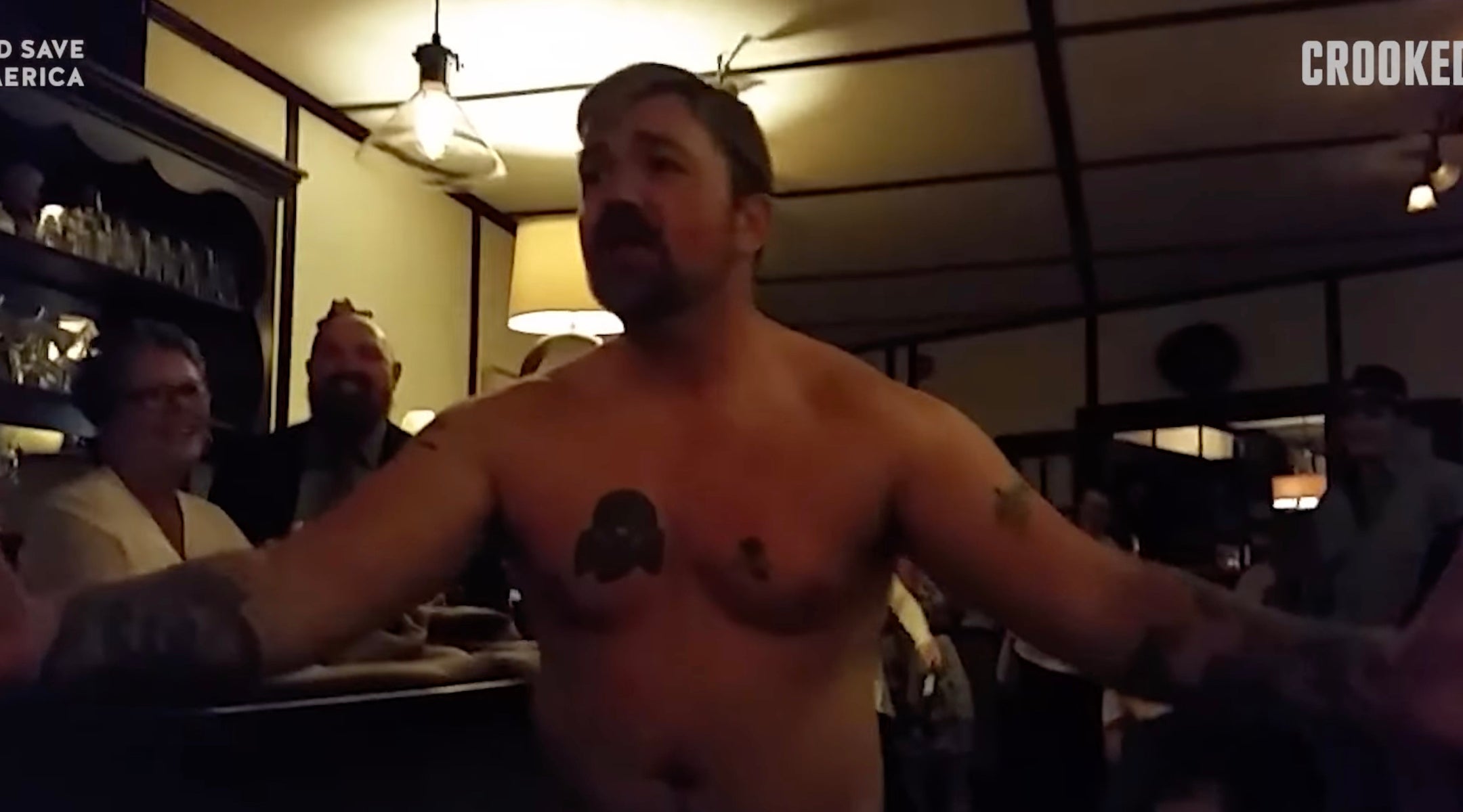 A shirtless man singing at a wedding with a Nazi tattoo
