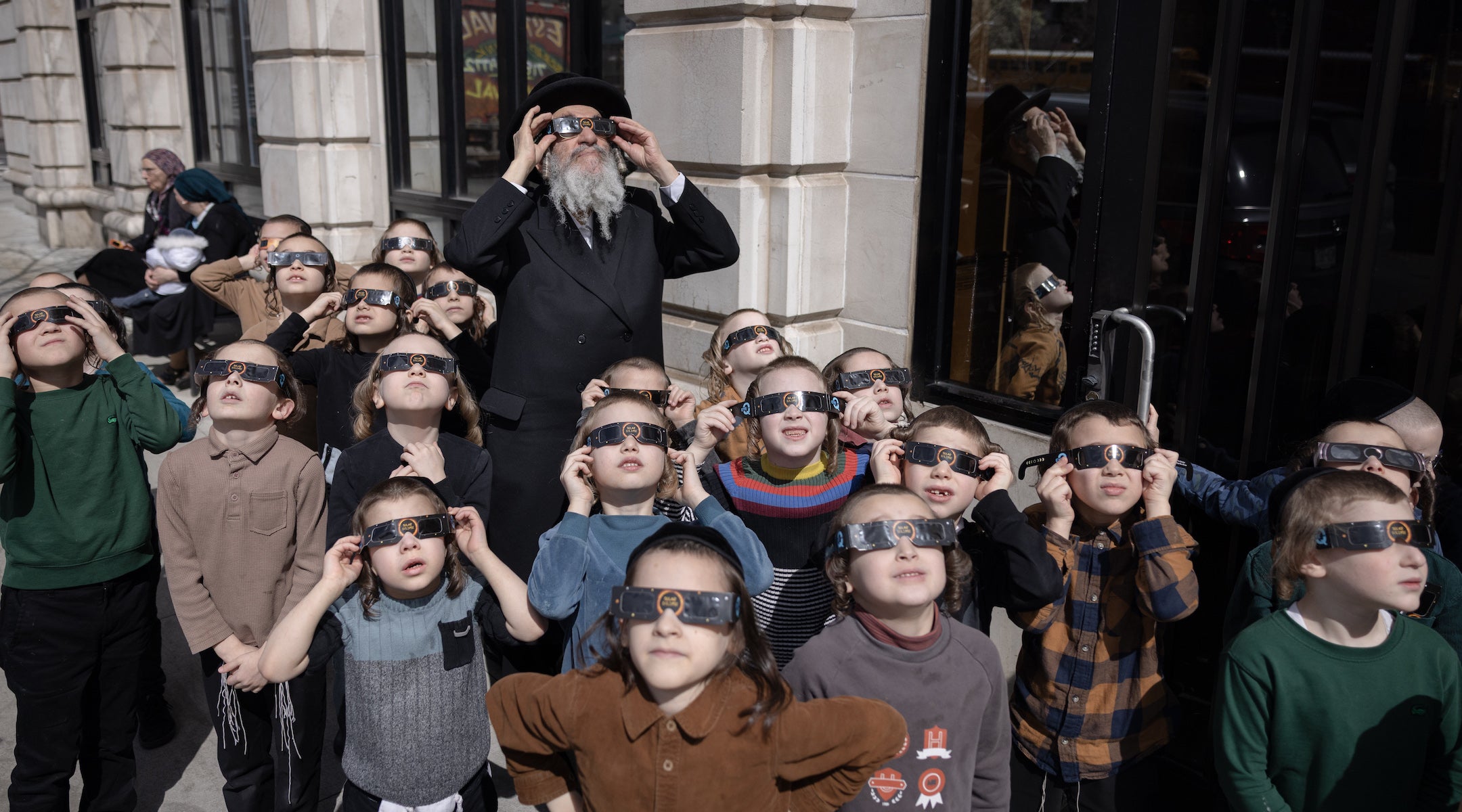 A photo of Hasidic children using solar eclipse glasses to view the solar eclipse.