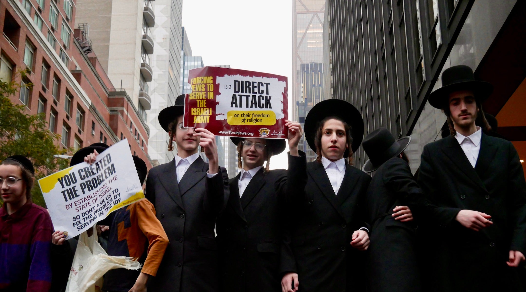 Haredi protesters hold signs protesting conscription in israel.