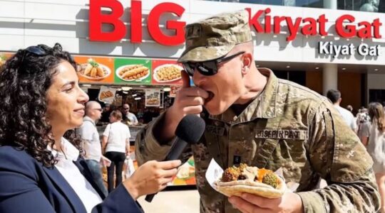 A photo of a soldier eating enxt to a reporter with a storefront behind them.